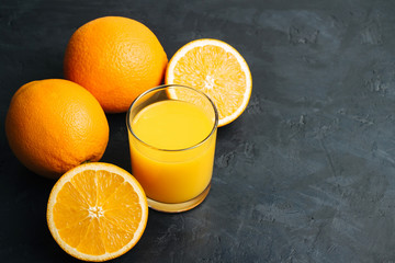 Orange fresh drink, glass of juice and ripe citrus fruits on a black, textured background