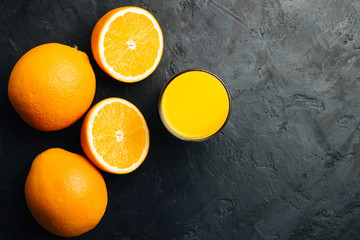 Orange fresh drink, glass of juice and ripe citrus fruits on a black, textured background, top view