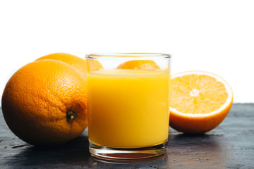 Orange fresh drink, glass of juice and ripe citrus fruits on a black, table and white background