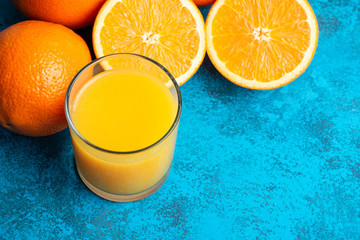 Orange fresh drink, glass of juice and ripe citrus fruits on a blue background