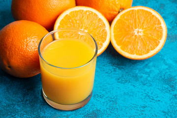 Orange fresh drink, glass of juice and ripe citrus fruits on a blue background