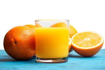 Orange fresh drink, glass of juice and ripe citrus fruits on a blue table and white background