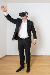 Mann steht im leeren Raum, er öffnet virtuelle Schränke und Schubladen dank VR Brille, hochkant