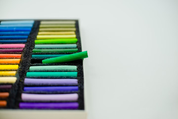 Fototapeta premium Close up view of bright colorful pastel chalks on white background. Set of multicolored pastel crayons in openartist box on a white background, top view.