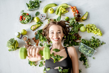 Beauty portrait of a sports woman surrounded by various healthy food lying on the floor. Healthy eating and sports lifestyle concept - obrazy, fototapety, plakaty