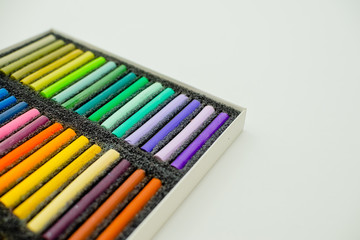 Close up view of bright colorful pastel chalks  on white background. Set of multicolored pastel crayons in openartist box on a white background, top view.