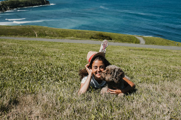 Fototapeta premium .Young and funny woman playing with her nice spanish water dog on a sunny summer morning in the north of Spain. Lying on the grass overlooking the sea. Lifestyle.