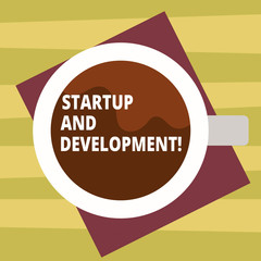 Text sign showing Startup And Development. Conceptual photo search for a repeatable and scalable business model Top View of Drinking Cup Filled with Beverage on Color Paper photo