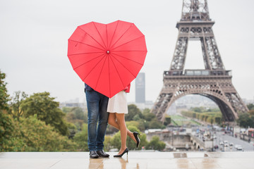 Romantic couple hiding behind heart shaped red umbrella in front of the Eiffel tower © Anna