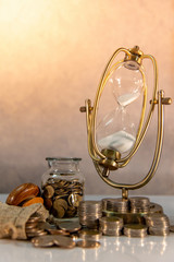 Sand running through the shape of hourglass with coins stack and currency jars on table. Time investment. Retirement saving concept. Urgency countdown timer for business payment deadline