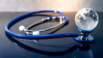 Global healthcare concept. World globe crystal glass on blue stethoscope on glossy desk. Health and...