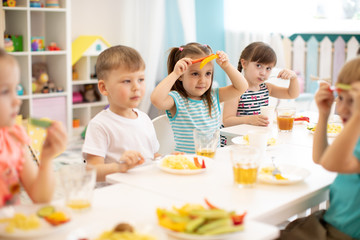 funny children eating vegetables in kindergarten or nursery