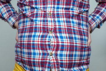 fat man in a plaid shirt is having trouble fastening his small clothes  with buttons; his bare belly is visible through the holes
