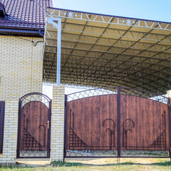 Brick house with a fence and gates. A large awning with a steel