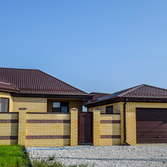 Brick house with a fence and gates. View of a new built-up fence