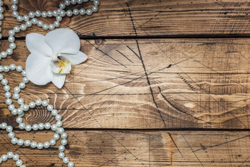 Orchid flower and beads on a wooden table. Concept romance mood. Copy space and flat lay