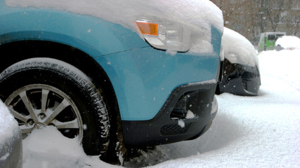 Car wheels stuck in snow drift. Wheel of blue passenger car is stuck in snow. Adverse weather conditions.