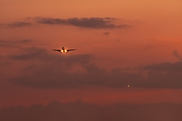 Commercial airline. Passenger plane landing at airport with beautiful sunset  sky and clouds. Arrival flight. Airplane flying in a line for landing. Aircraft open light in the evening flight.