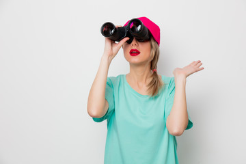 Beautiful young girl in pink cap and blue t-shirt looking for something with binocular on white background.