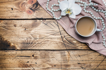 Orchid flower, cup of coffee and beads on a wooden table. Concept romance mood. Copy space and flat lay