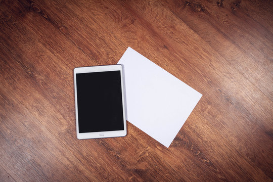 White tablet pc with paper sheet on wooden background