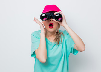 Beautiful young girl in pink cap and blue t-shirt looking for something with binocular on white background.
