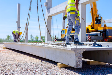 Worker is attaching crane hooks to concrete joist
