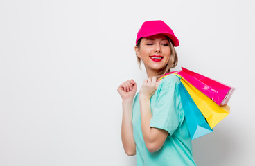 Beautiful young girl in pink cap and blue t-shirt with shopping bags on white background.