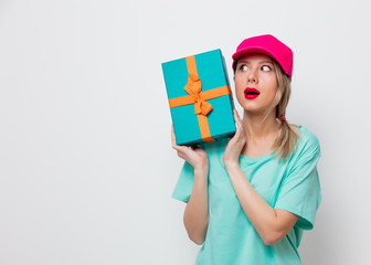 Beautiful young girl in pink cap and blue t-shirt with holiday present box on white background.