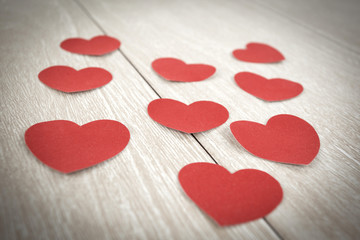 red paper hearts on light wooden background.