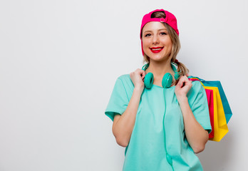 Beautiful young girl in pink cap and blue t-shirt with shopping bags on white background.