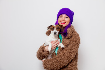 Beautiful young girl with purple hair in jacket holding dog on white background.