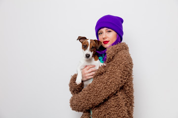 Beautiful young girl with purple hair in jacket holding dog on white background.