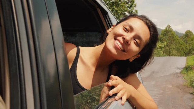 Happy Young Mixed Race Woman Leaning Out Side Car Window, Looking Around, Smiling and Enjoying Warm Summer Headwind. 4K Slowmotion. Bali, Indonesia.