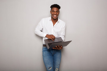 Obraz na płótnie Canvas happy young black man holding laptop computer by gray wall