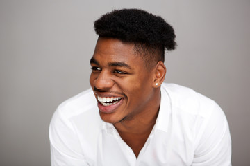 Close up handsome young african american man laughing and looking away against gray background