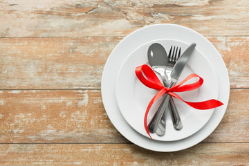 valentines day and festive dinner concept - plate with spoon, knife and fork tied with red ribbon on wooden table from top