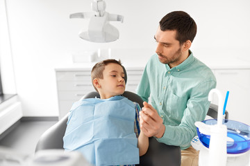 medicine, dentistry and healthcare concept - father supporting son at dental clinic