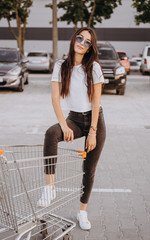 Young and happy woman put leg inside a shopping cart