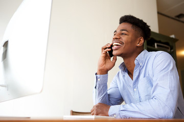 smiling young african american businessman talking on phone while looking at computer