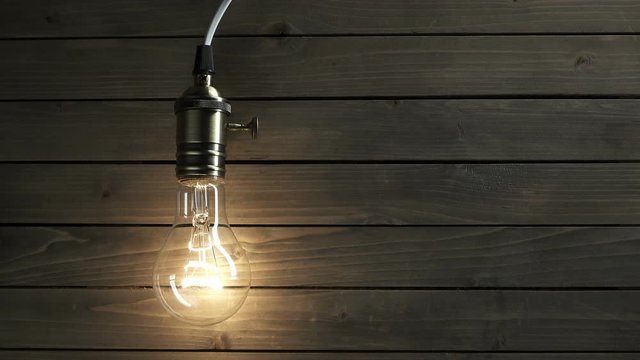 The light bulb slowly lights up, quickly flickers on a background from a wood