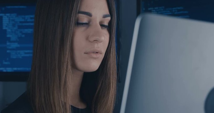 portrait of young woman programmer working at a computer in the data center filled with display screens