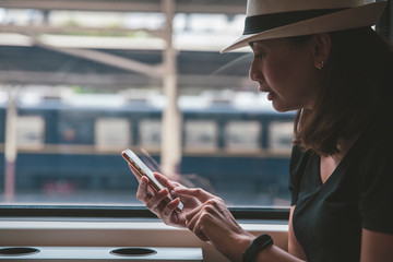 Beautiful young woman traveler using smartphone at a train station , Transportation and travel lifestyle concept