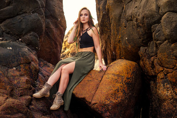 portrait of stylish elegant redheaded chestnut blonde young girl in indie bohemian bo-ho style clothes black stylish top.boho woman long hair,makeup and green feathers in head on the rocks by the sea