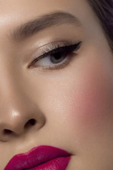 Fototapeta premium Close-up beauty of a half female face with creative fashion evening make-up. Black arrows on the eyes and extremely long eyelashes, on plump lips matte pink lip color. Well-groomed skin after spa