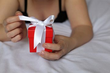 Woman in bra opens gift box on the bed, Valentine's day morning. Romantic present for birthday or anniversary