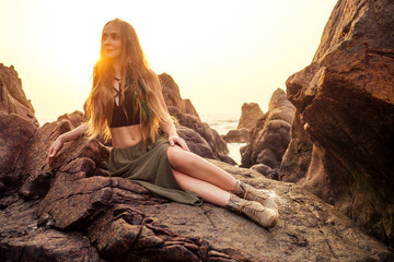 fashion hippie model portrait outdoors boho style young flower children woman with headdress made of feathers in a brown long skirt and black top dress,stylish shoes boots on stone Arambol Goa beach