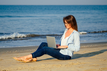 exchange student woman in glasses using laptop freelancing on the tropical paradise beach. Girl freelancer work sitting in a summer sand on the seashore remote work indian ocean copyspace success