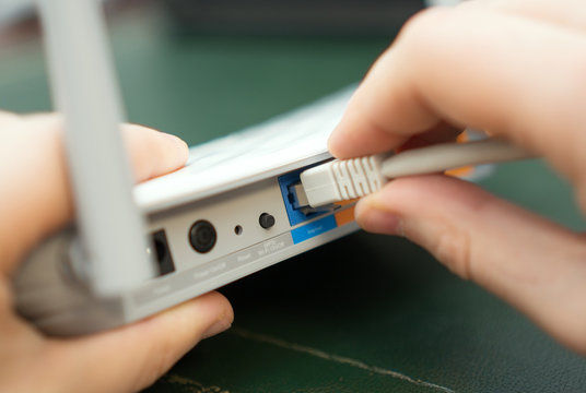 Man Plugging Internet Cable Into Wifi Router.