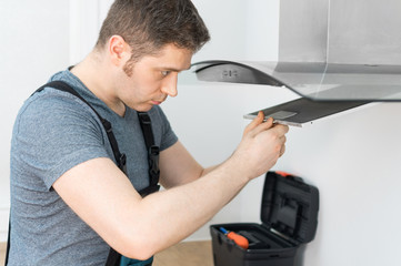 Handsome foreman fixing exhaust hood in the kitchen.